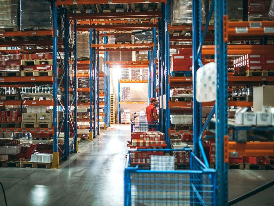 retail warehouse with orange and blue shelves and stanchions worker in distance