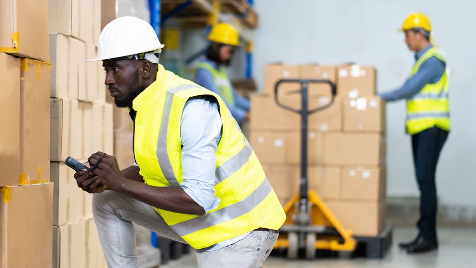 african-american man in safety gear kneeling in warehouse
