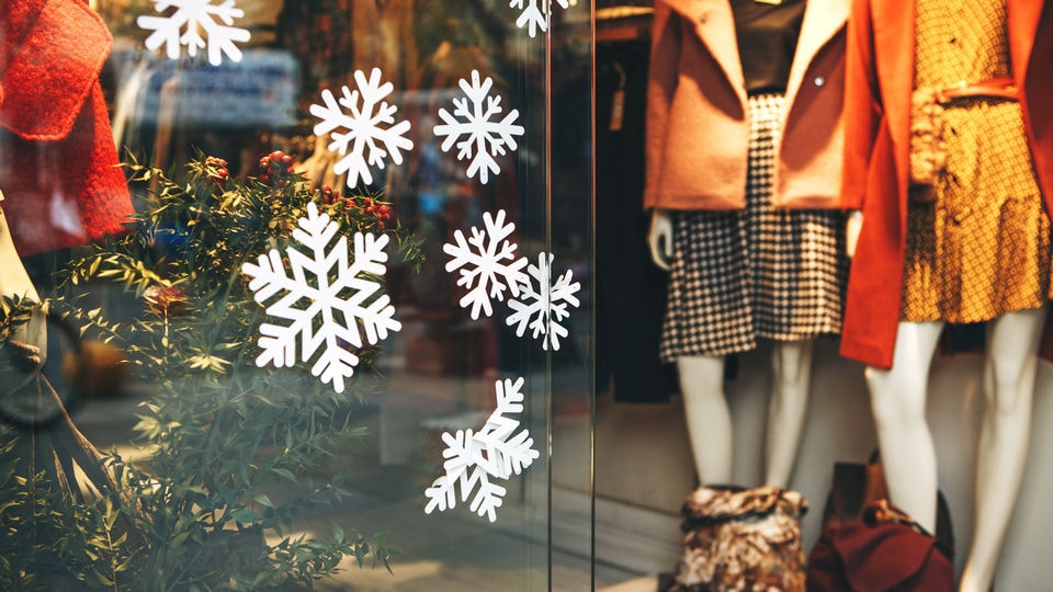 retail store window with mannequins in fall colors and paper snowflakes on the glass
