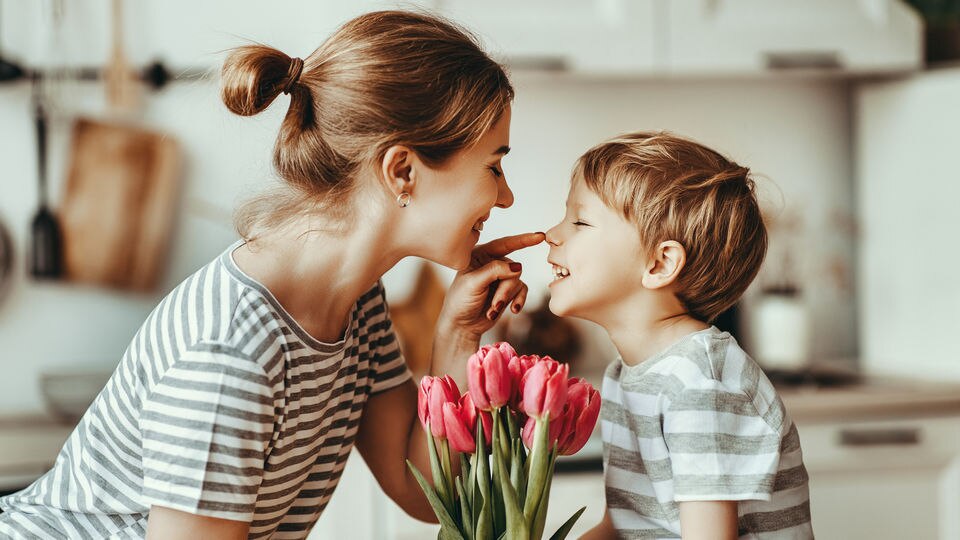 young mother and son sharing a playful moment with a bunch of pink tulips in the foreground