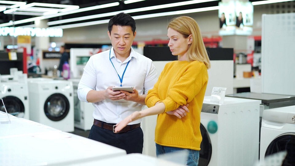 male sales associate with electronic device assisting female shopper in home appliance department of diy store