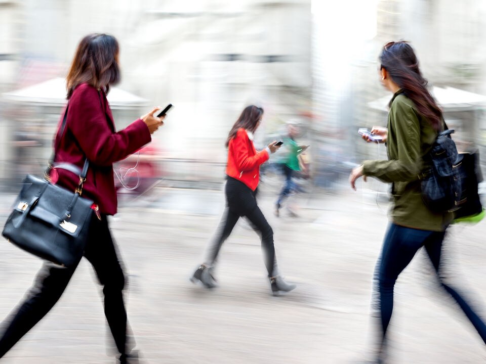 3 women walking on the street and using their cell phones against a blurred urban background