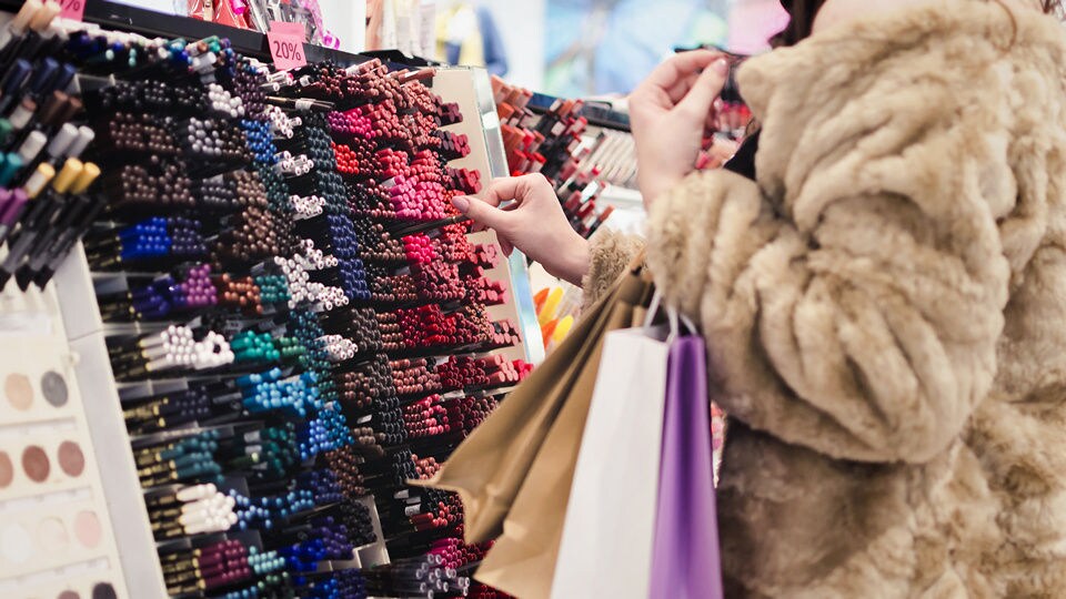 female shoppin wearing faux fur coat in a retail health and beauty store comparing colors of makeup