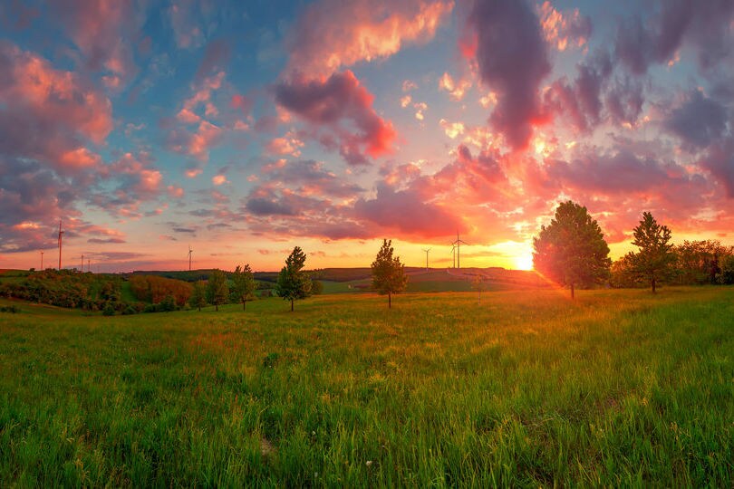 sunset over rural home with large fields of gass and scattered trees around the house with the sky a deepening blue and rose orange and gold tints to the clouds