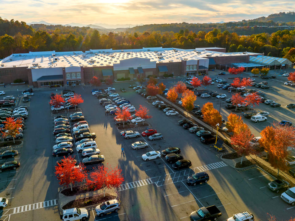 aerial view of busy shopping mall parking lot with retail store entrances and autumn leaves