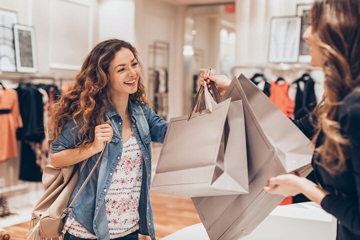 female sales associate handing two shopping bags to female customer at retail counter