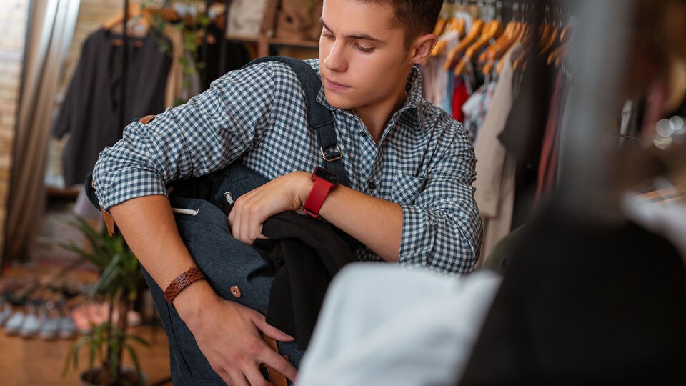 young male shoplifter in retail apparel store putting items in his backpack with the intent to steal