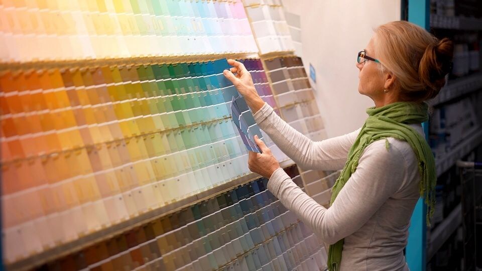 middle age female shopper wearing green scarf looks through a paint chip display in a retail hardware store