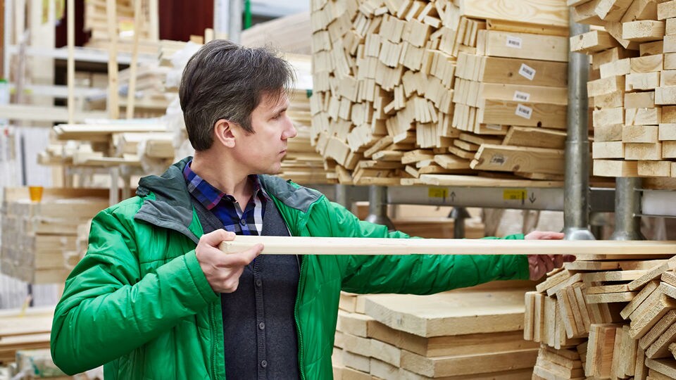 adult male wearing green jacket in retail hardware store lumber department inspecting a long strip of wood
