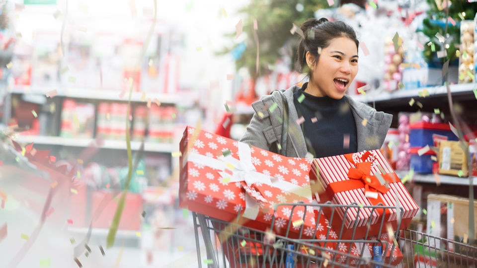 female pushing shopping cart with wrapped gifts through year-end holiday decorated retail store