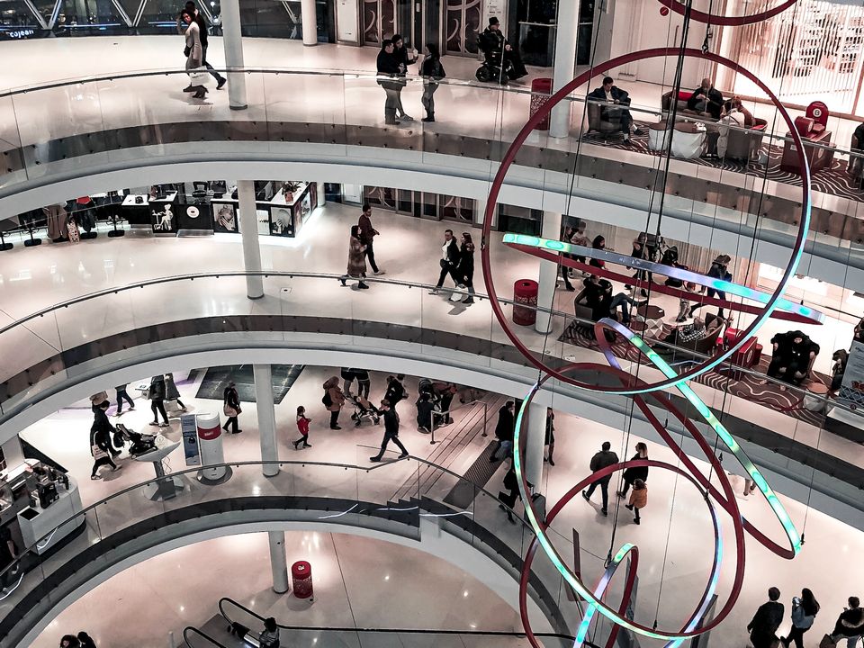 interior of multi-level shopping mall with many retail shoppers and a large hanging sculpture of interlocking rings