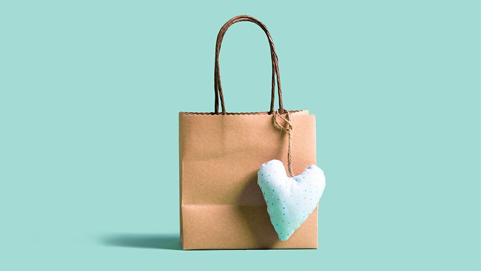 brown paper retail shopping bag with plush heart attached against teal colored background