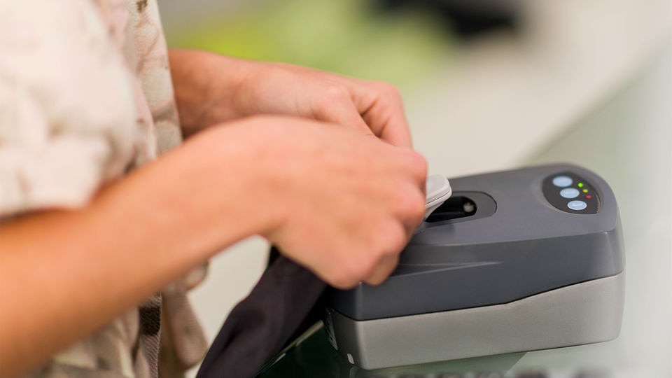 store associate using hard tag detacher to remove eas loss prevention tag in retail checkout