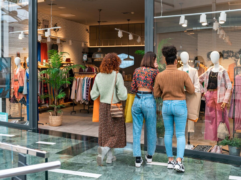 3 female shoppers in a shopping mall looking at a store display inside a retail apparel store display