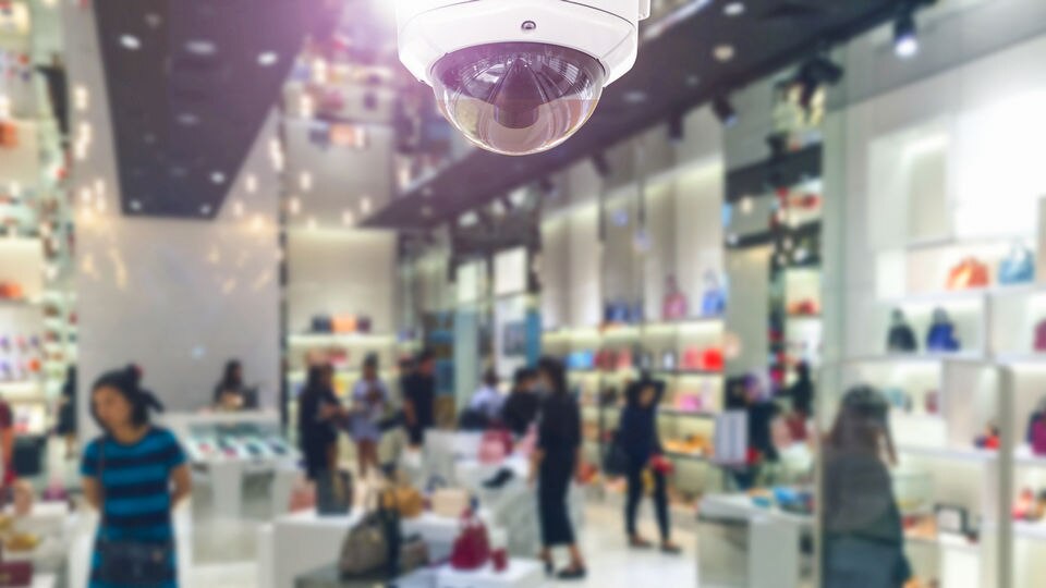 wide angle view of interior of apparel and accessories retail store with shoppers out of focus and ceiling mounted computer vision surveillance camera