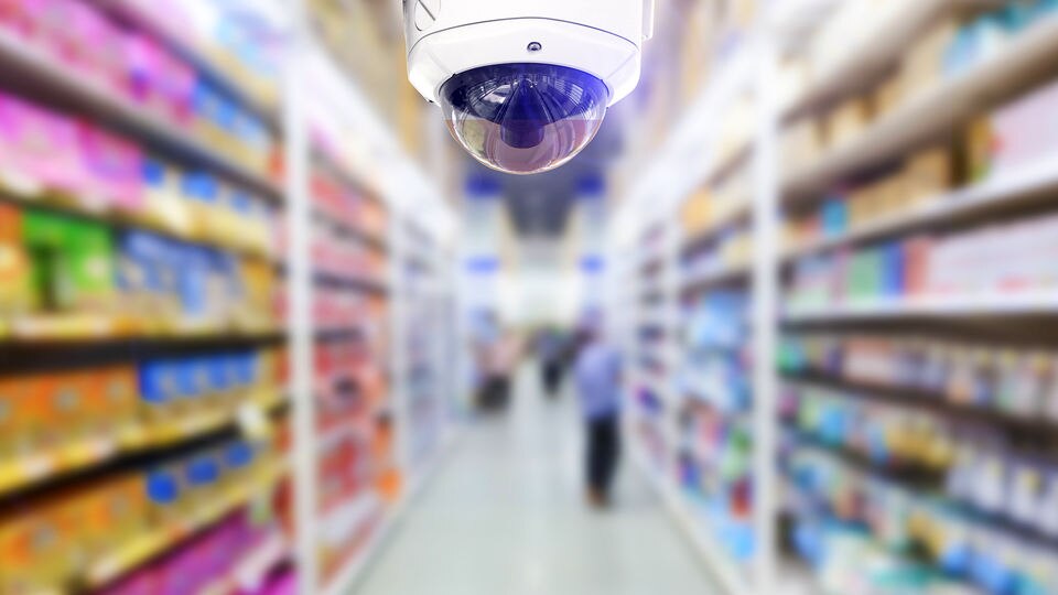 ceiling mounted 360 degree ip surveillance camera in busy retail store in front of blurry background of shoppers and shelves