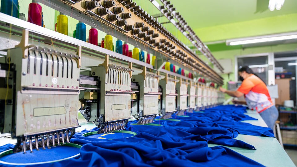 female garment worker tending to a sewing machine making apparel items in a textile factory
