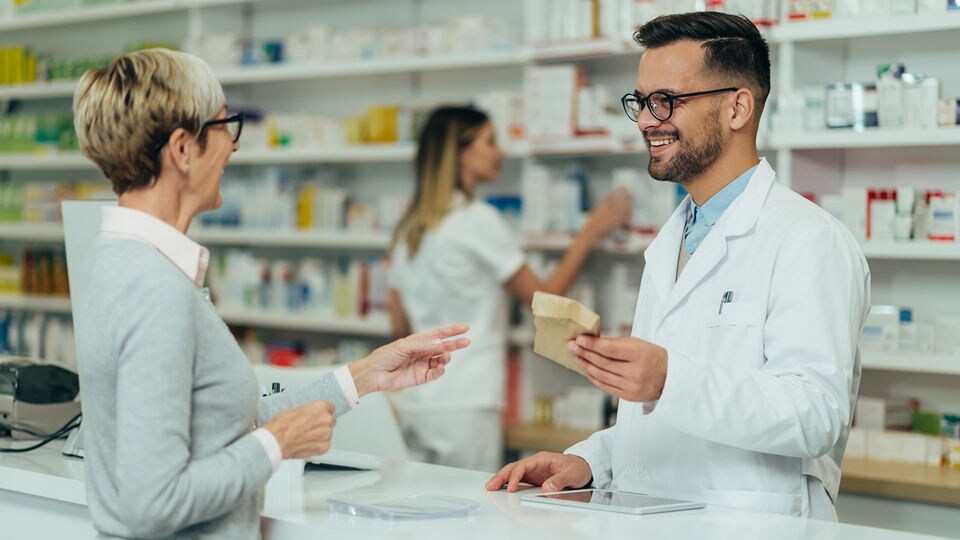 male pharmacist handing a package across the counter to a senior female shopper