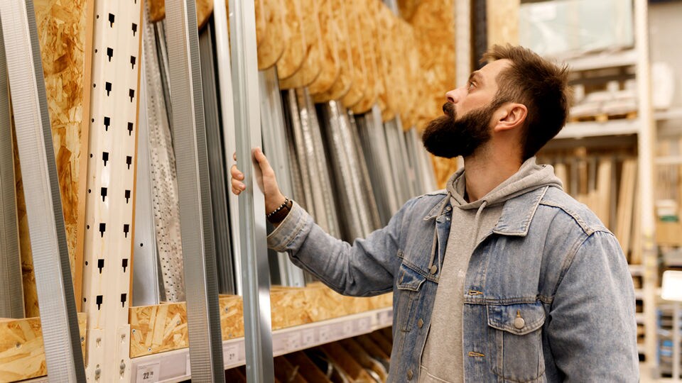 bearded male shopper in denim jacket looking at construction materials in a retail hardware store