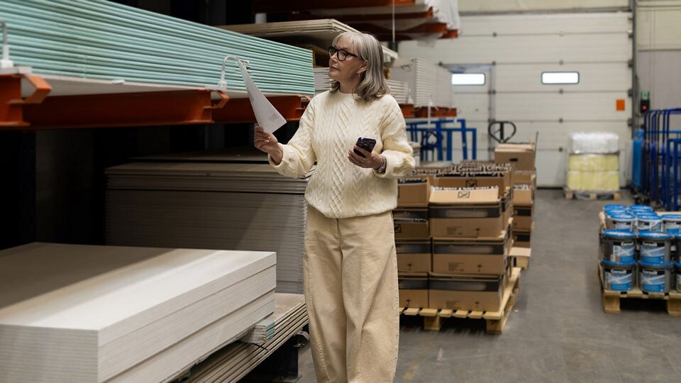 senior woman in retail hardware store looking at construction supplies with a list in one hand and a cell phone in the other