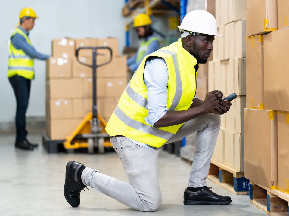 retail warehouse worker checks carton details with tablet with other workers performing tasks in the background