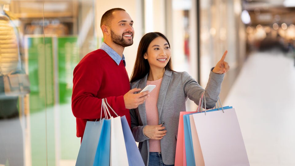 male female mixed race couple carrying shopping bags in retail mall viewing information on phone screen