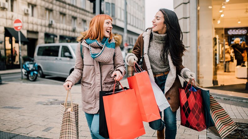 two female shoppers carrying shopping bags leaving retail store