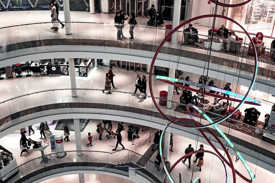 interior of multi-level shopping mall with many retail shoppers and a large hanging sculpture of interlocking rings