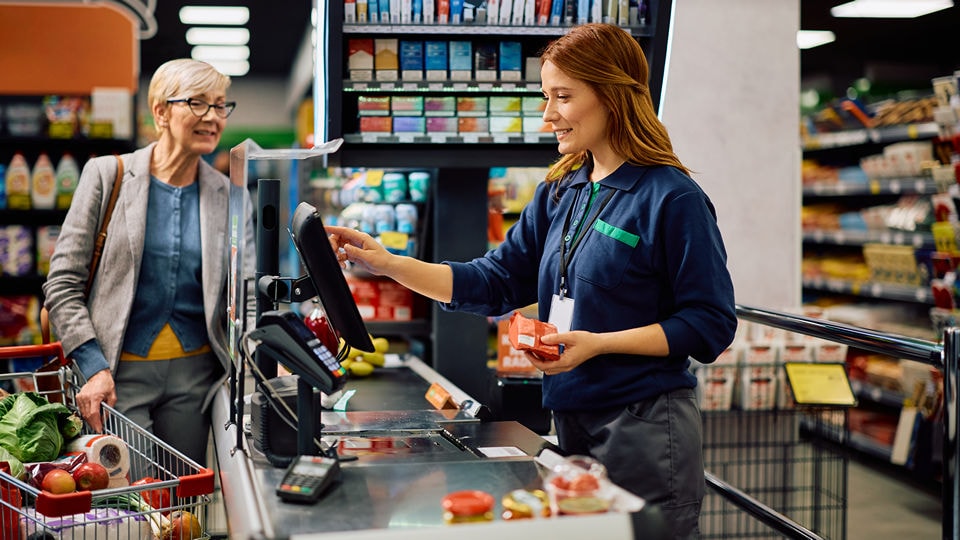 young woman cashier helps older woman to checkout at the retail grocery store