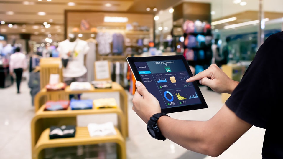 retail associate reviews store management dashboard on a tablet while looking at busy retail apparel shop