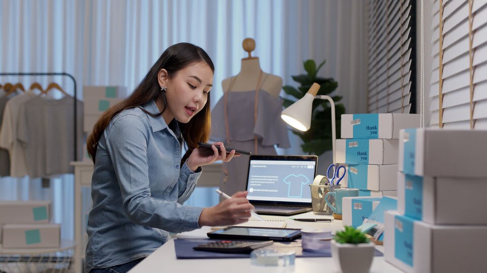 retail store employee talking on phone and working on omnichannel fulfillment packaging and working on laptop