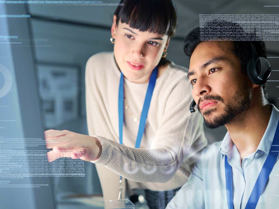 man and woman data analysts reviewing screen of retail data overlaid by lines and blocks of computer code