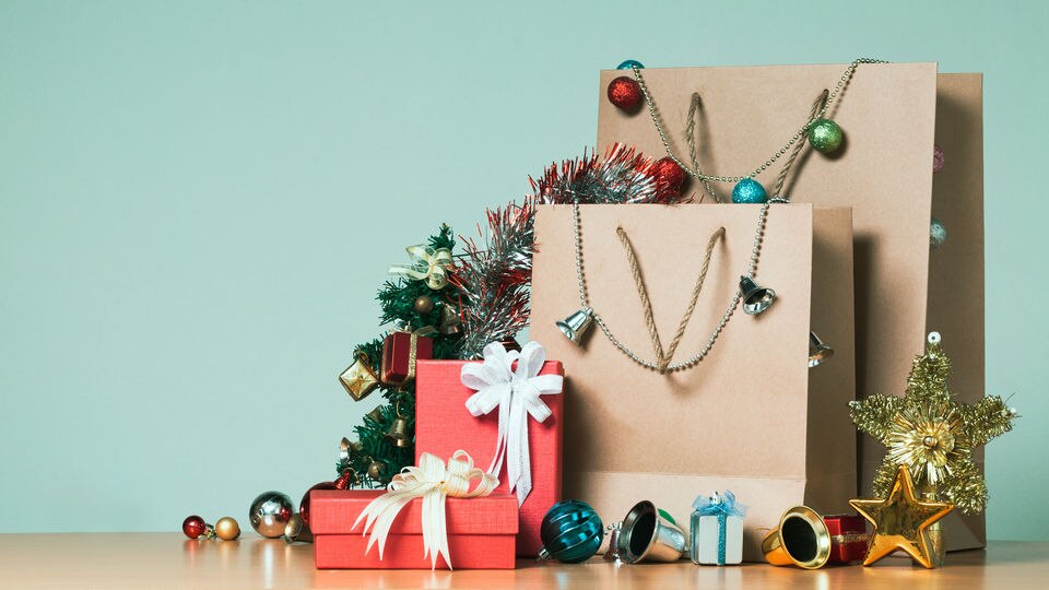 wrapped presents and retail shopping bags with christmas holiday decorations on a table in front of a light blue green wall