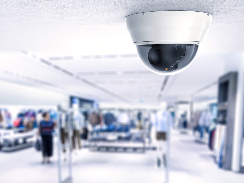 ceiling-mounted dome video surveillance counter in foreground blurry retail apparel store in background