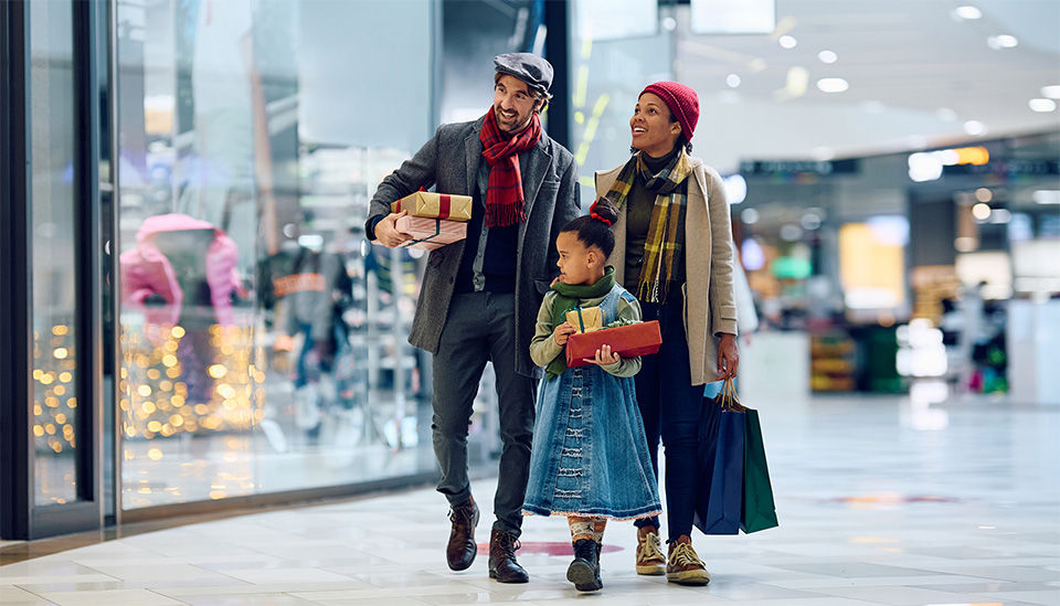 family of male female and young girl in warm clothing shopping for christmas season in a retail shopping mall carrying their purchases