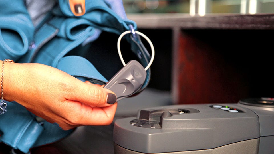 hand of female sales associate using sensormatic detacher to remove a supertag lanyard tag from an apparel item