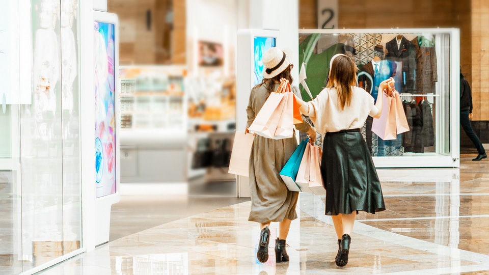 two female shoppers walking in retail shopping center carrying shopping bags