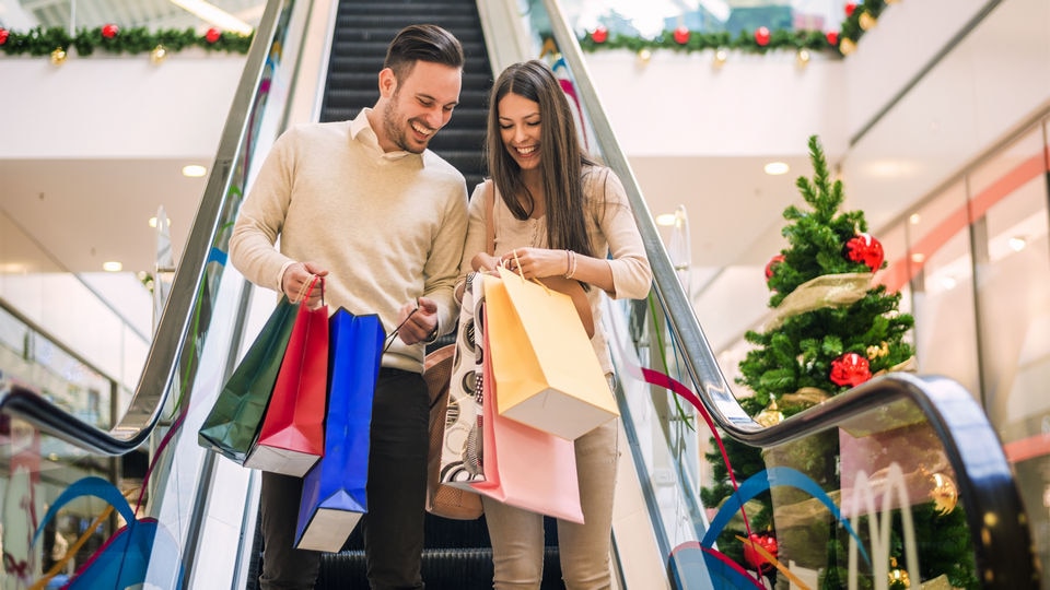 loving male female couple with many shopping bags descending on escalator in retail shopping mall decorated for winter holidays