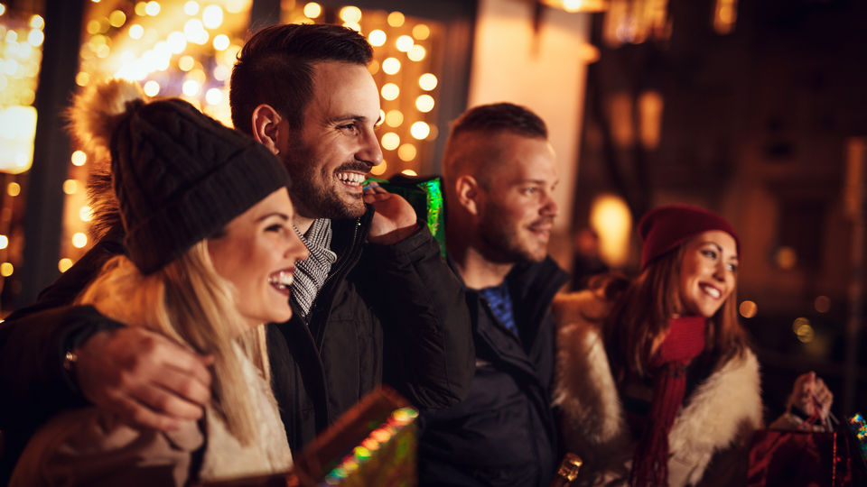 group of four friends two men and two women in a retail shopping area decorated for holiday season