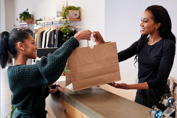 female retail associate handing shopping bag to female customer