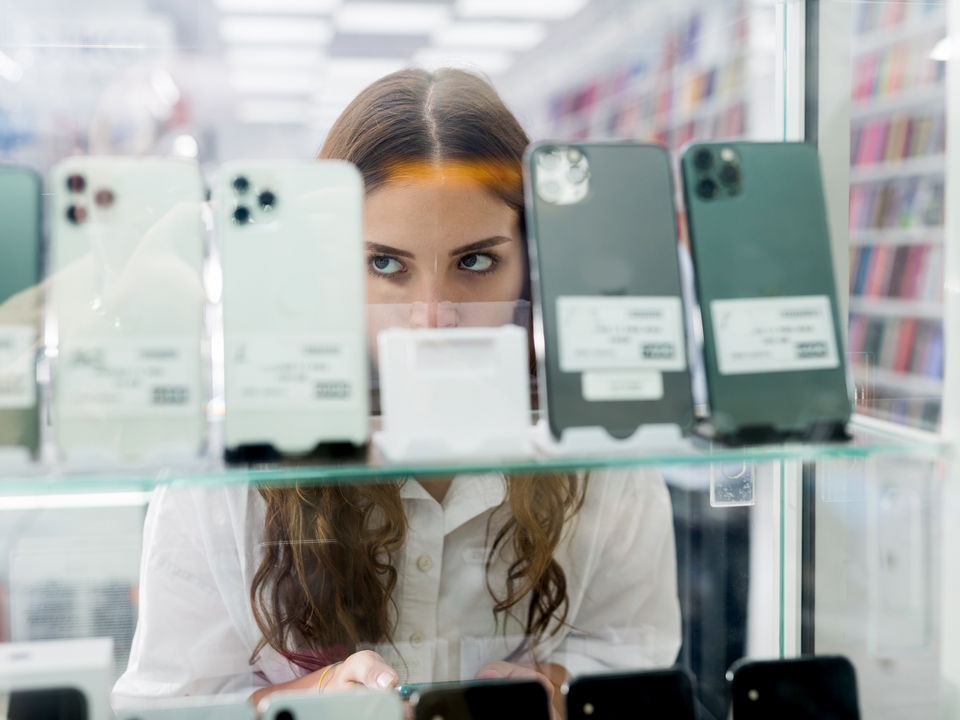 woman shoplifter face partially obscured by display of mobile phones in retail electronics store