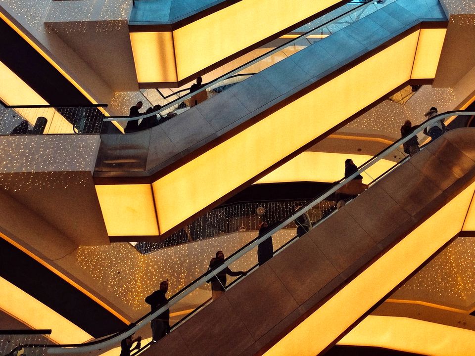 looking up in multi-level shopping mall at three flights of crowded escalators underlit with golden lighting