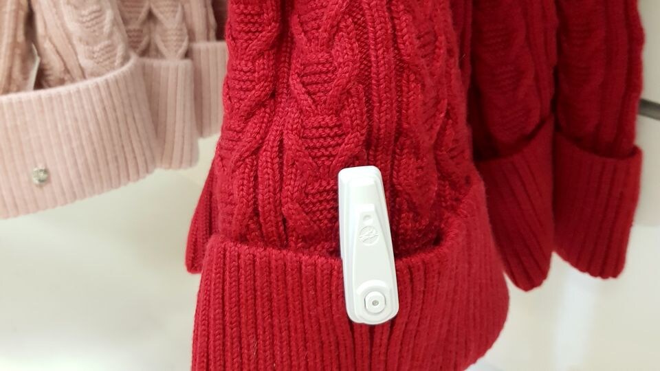 sensormatic infuzion hard tag attached to red sweater sleeve in retail apparel store