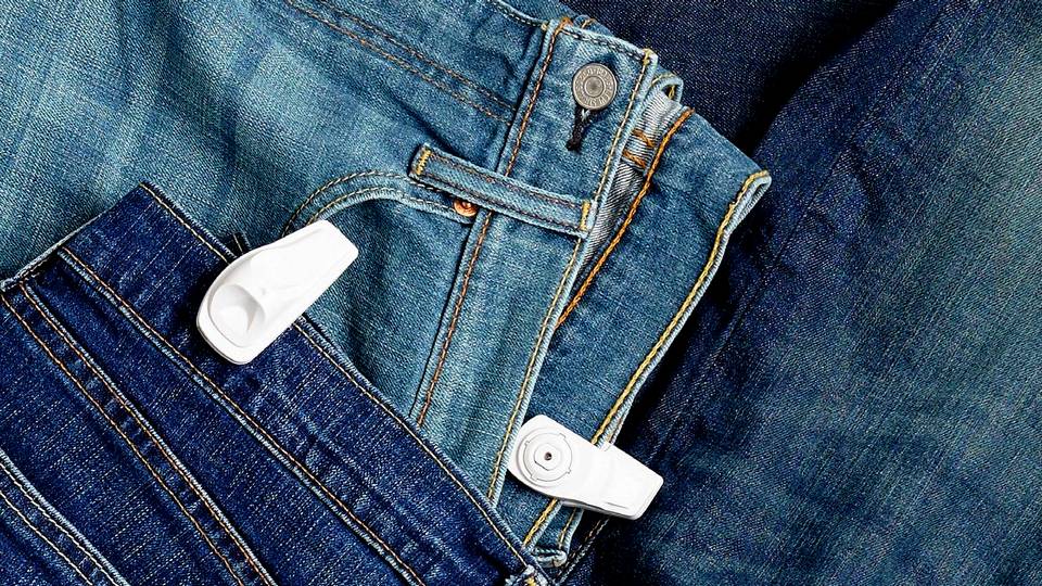sensormatic infuzion super tags attached to several pairs of jeans in a retail apparel store display