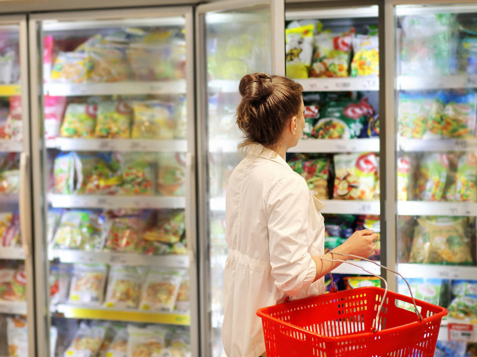 female shopper in retail grocery store carrying  handheld food basket viewing frozen food case
