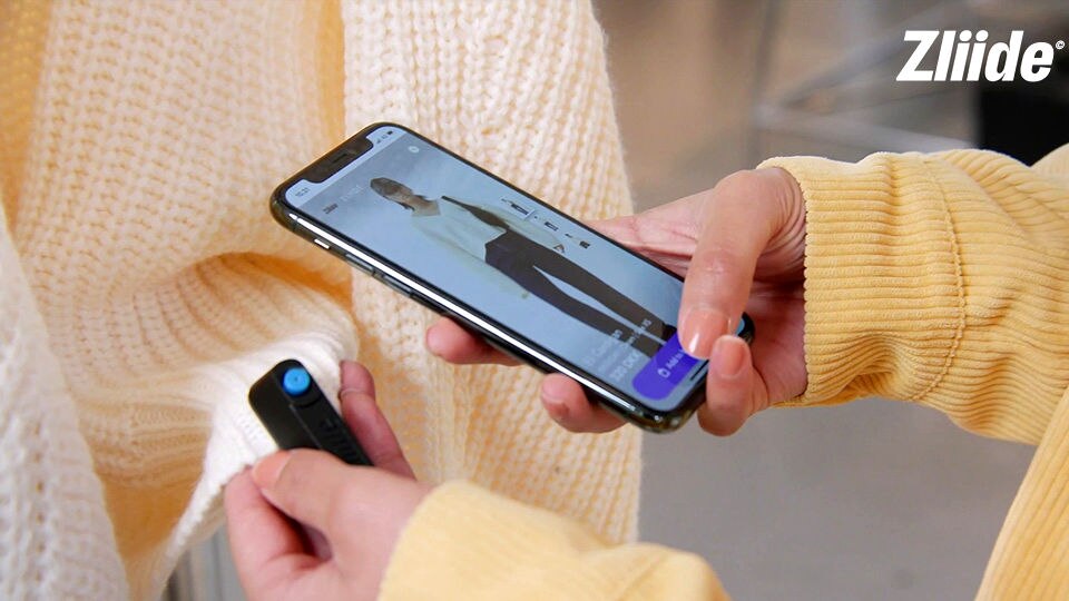 female shopper in yellow sweater viewing retail purchase on smartphone while holding hard tag on purchased garment