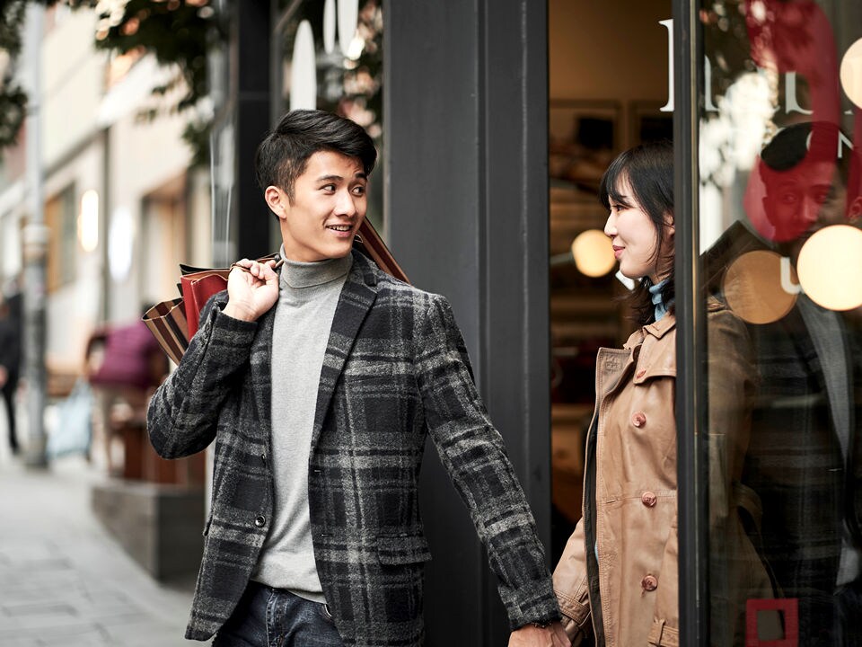male and female couple carrying shopping bags stepping out of retail store onto busy shopping street