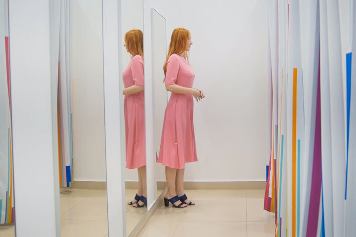 woman partially reflected in full-length fitting-room mirrors