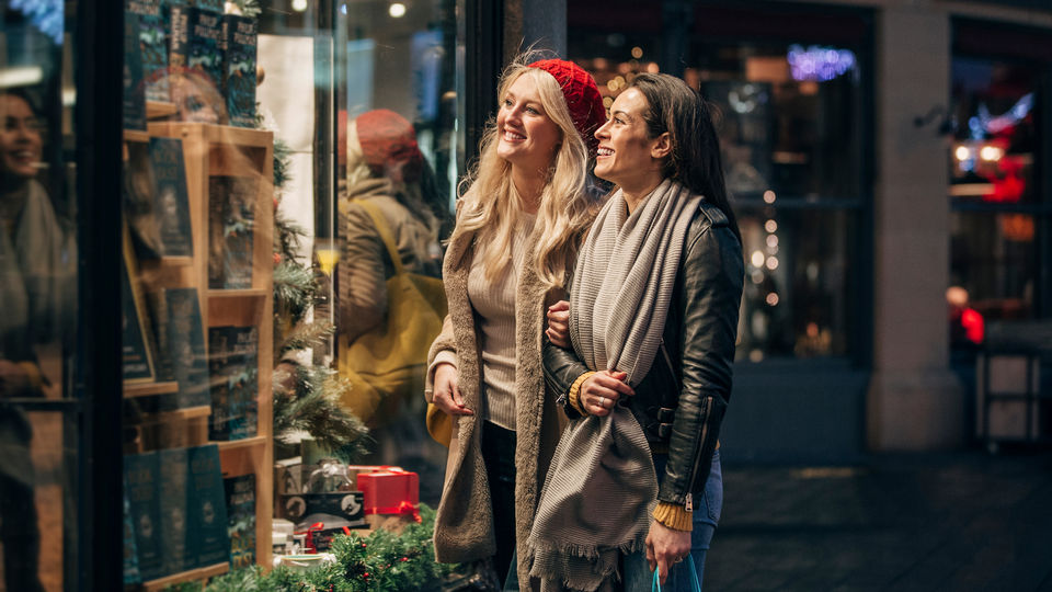 two female shoppers outside holiday decorated retail store looking in display window
