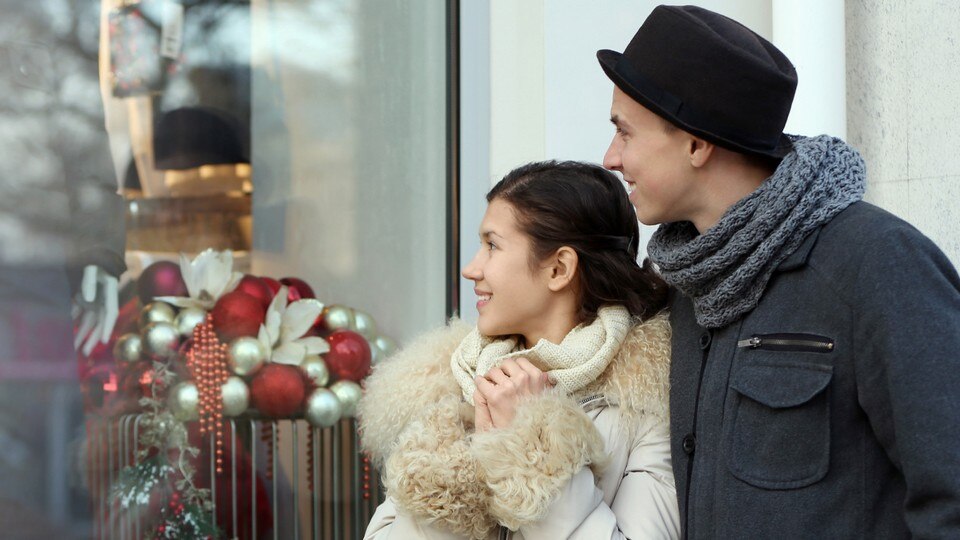 male female couple shoppers dressed in winter outerwear outside retail store decorated for holiday